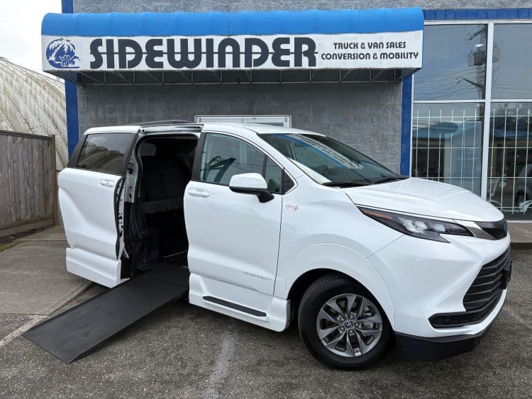 White Toyota Sienna parked in front of the Sidewinder Truck & Van Sales storefront in Chilliwack, passenger sliding door open and the VMI Northstar in-floor ramp deployed onto the pavement