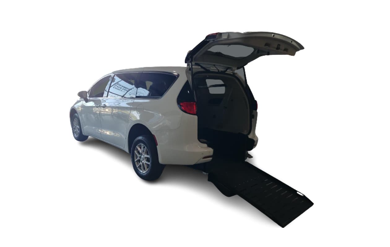 White Chrysler Grand Caravan with the Sidewinder rear-entry conversion, rear three-quarter view, liftgate raised and the manual foldout ramp extended to the ground